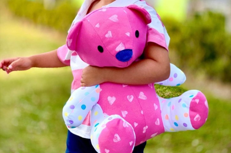 young child holding pink and white bear outside